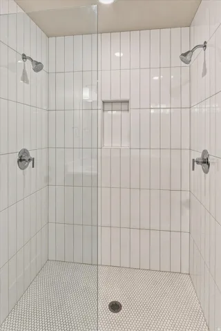 Shower enclosure featuring white vertical subway tile, dual shower heads, a built-in shower niche, and white hexagonal mosaic floor tiles