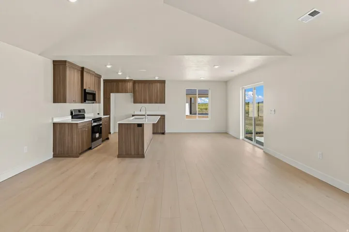 Open-concept kitchen and living area featuring light wood-finish flooring, vaulted ceilings, and recessed lighting