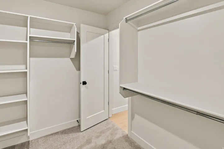 Walk-in closet featuring white built-in shelving, multiple hanging rods, and light gray carpeting
