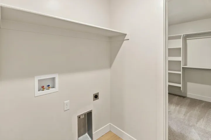 Dedicated laundry area with utility hookups and an integrated shelf, featuring light-colored walls and wood-finish flooring