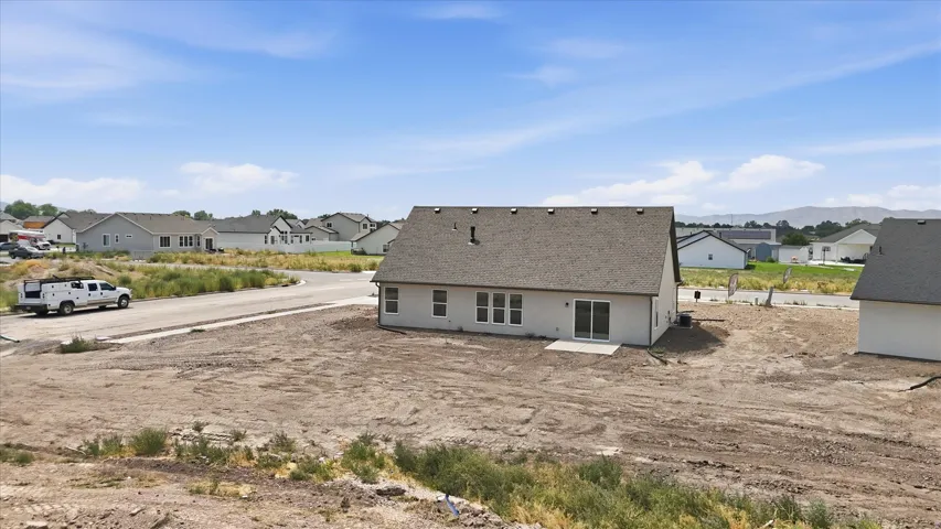 Newly constructed residence featuring a light-colored stucco exterior, a dark shingle roof, and multiple rear windows