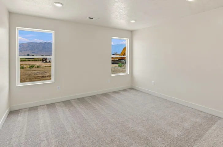 Spacious room with plush gray carpeting, white walls, two large windows, recessed lighting, and mountain scenery visible through the windows