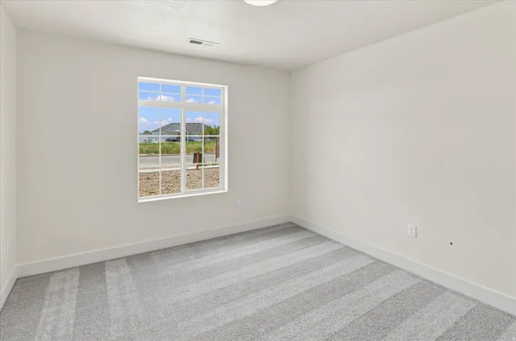 White-painted interior room featuring a multi-pane window with white trim, light-toned walls, gray patterned carpeting, and white baseboards