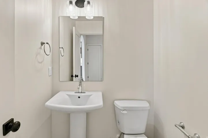 Pedestal sink with chrome faucet, complemented by a rectangular mirror and a two-light vanity fixture