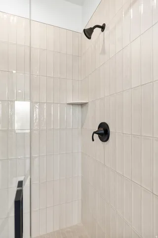 Shower enclosure featuring vertical-stacked white subway tile, matte black fixtures, a built-in shelf, and a glass panel door