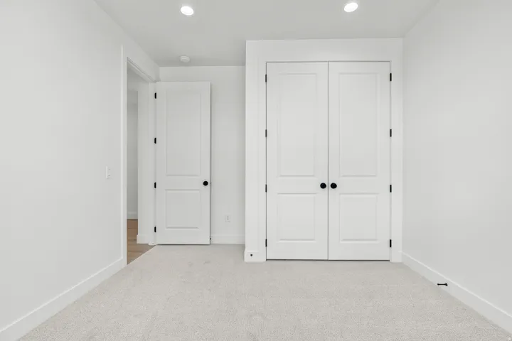 Room with light gray carpeting, crisp white walls, recessed lighting, and a double-door closet with matte black hardware