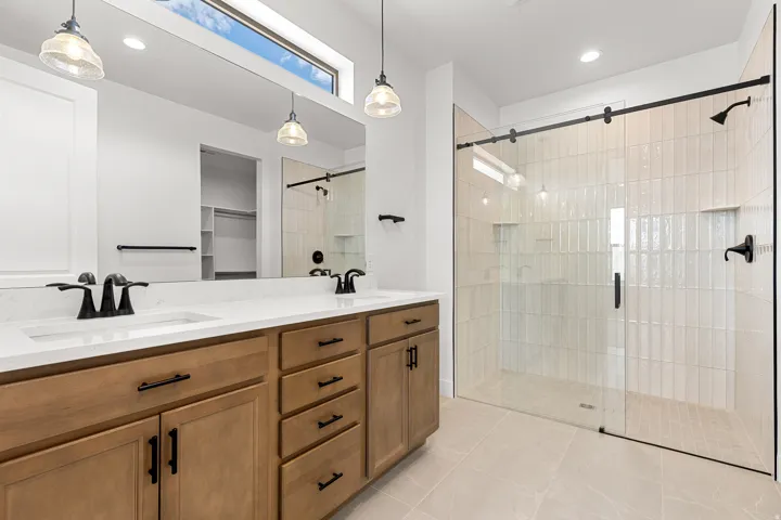Bathroom featuring a dual vanity with wood-finish cabinetry, white countertops, and matte black fixtures