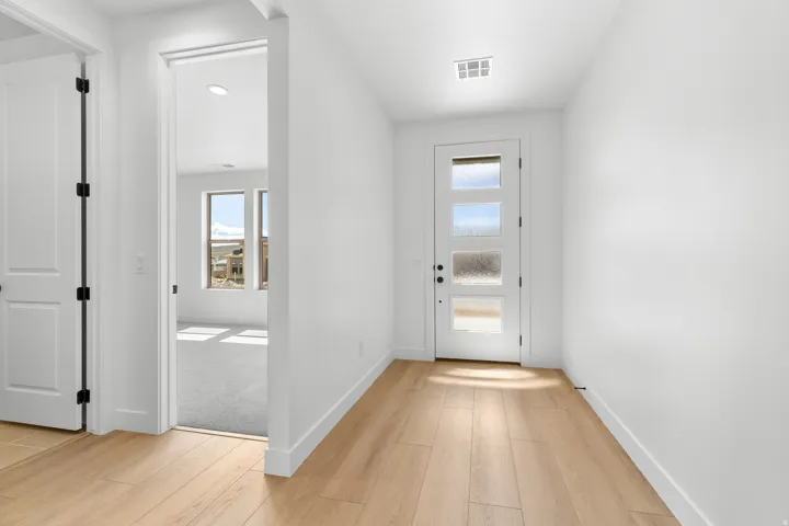 Entryway featuring light wood-finish flooring, a contemporary front door with frosted glass panels, and crisp white walls