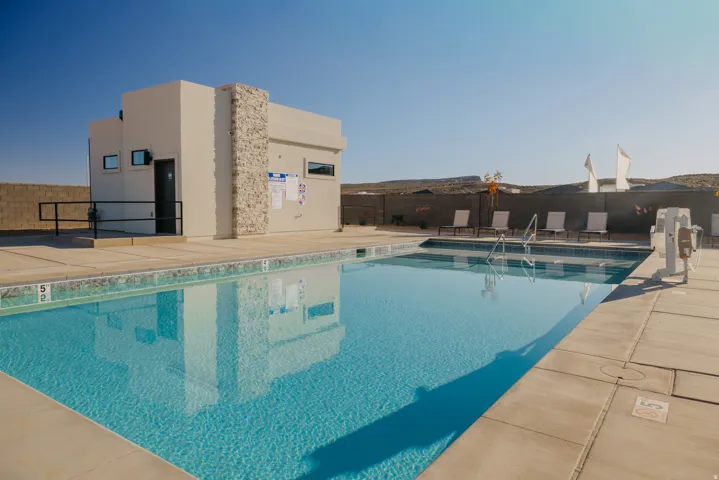 Outdoor swimming pool with concrete decking, a pool house featuring stone accents, and a surrounding privacy wall