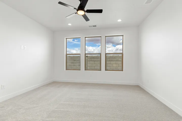 Spacious room featuring light-colored carpeting, white walls, and a ceiling fan with integrated lighting