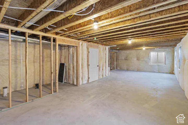 Unfinished basement featuring exposed wood joists, concrete flooring, framed wall sections, and multiple windows with horizontal blinds