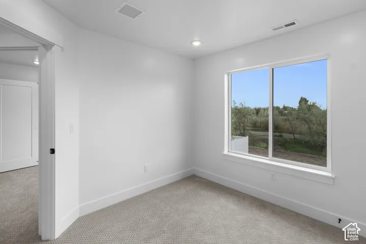 Carpeted room featuring a large window with white trim, recessed lighting, white walls, and white baseboards