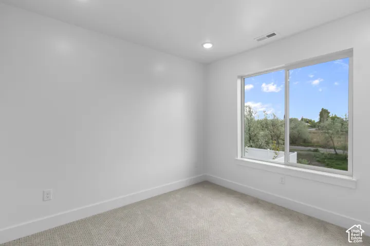 Bright interior space featuring a large window with white trim, recessed lighting, neutral carpet, and white baseboards