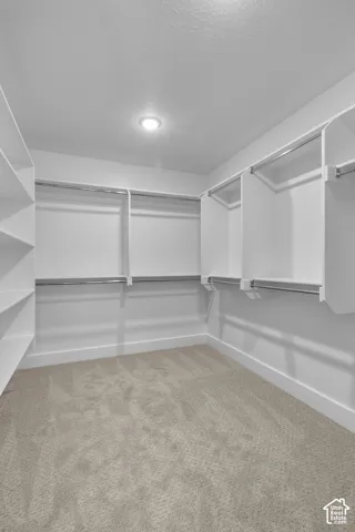 Walk-in closet featuring built-in white shelving, chrome hanging rods, recessed ceiling lighting, and neutral tone carpeting