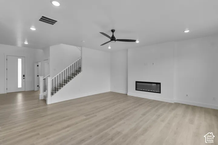 Spacious living area featuring wood-finish flooring, a contemporary electric fireplace, and a ceiling fan