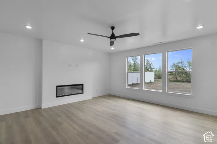 Spacious living area featuring contemporary wood-finish flooring, a linear electric fireplace, and recessed ceiling lighting
