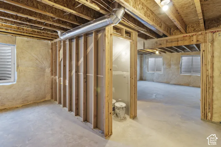 Unfinished basement featuring exposed wood joists and subflooring, framed wall sections, concrete flooring, two windows with horizontal blinds, and a visible duct system