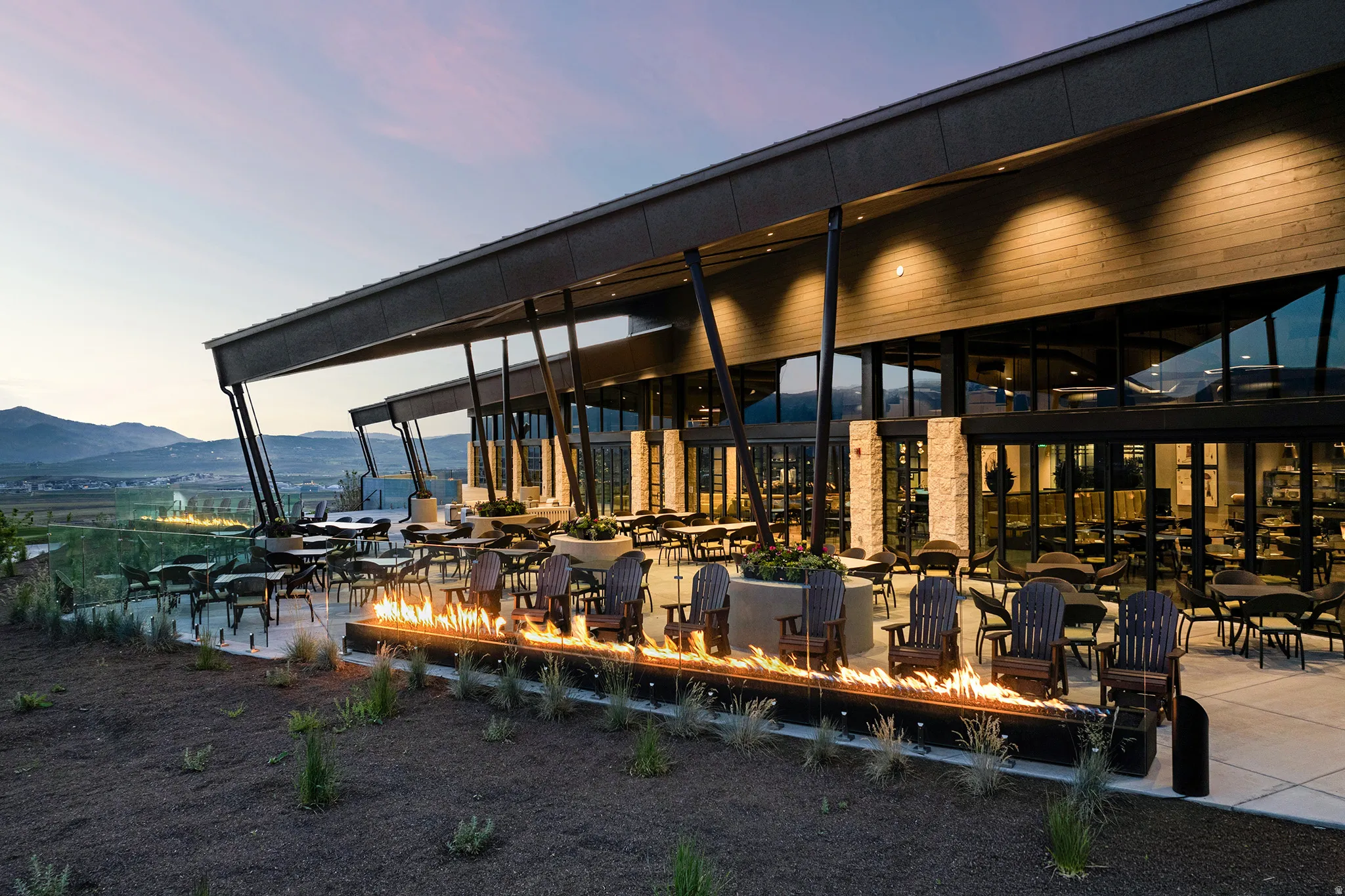 Spacious outdoor patio area featuring a linear fire pit, modern Adirondack chairs, and multiple dining arrangements