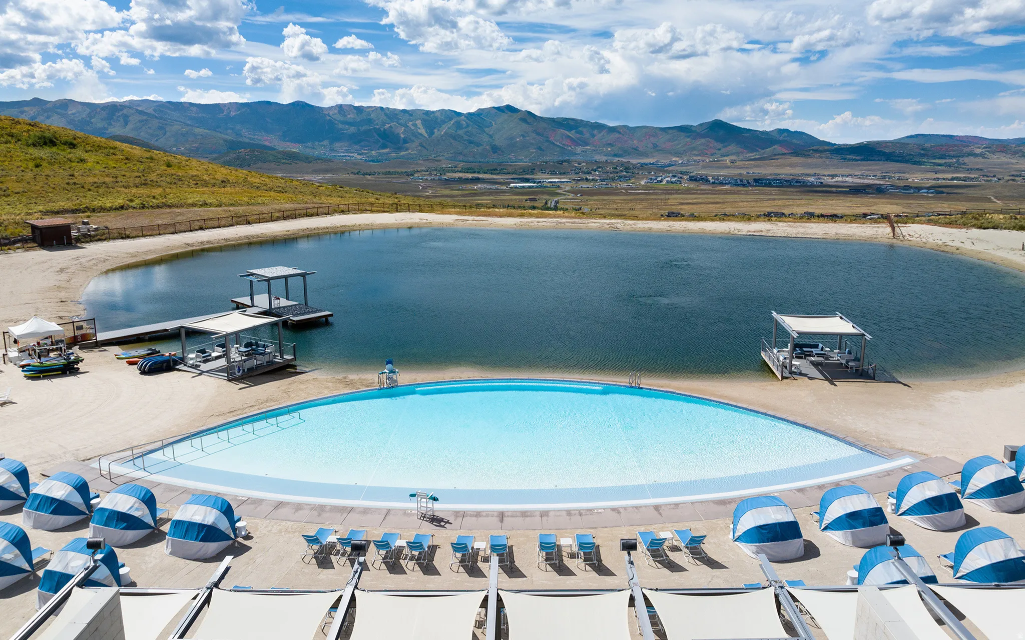 Expansive outdoor aquatic area featuring a large lagoon, a crescent-shaped pool with a zero-entry edge, multiple docks, and sandy shores