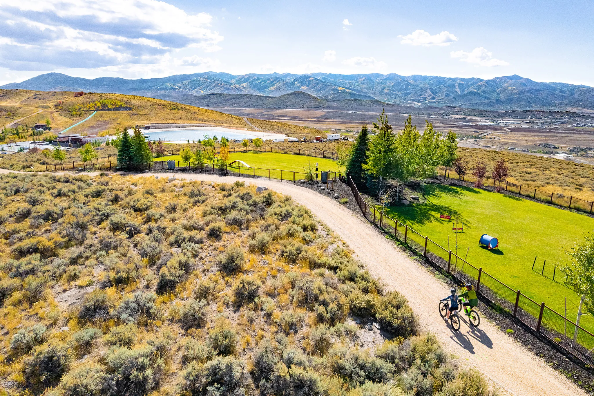 Expansive property featuring a gravel path, a manicured green lawn, and mature trees with distant mountain scenery