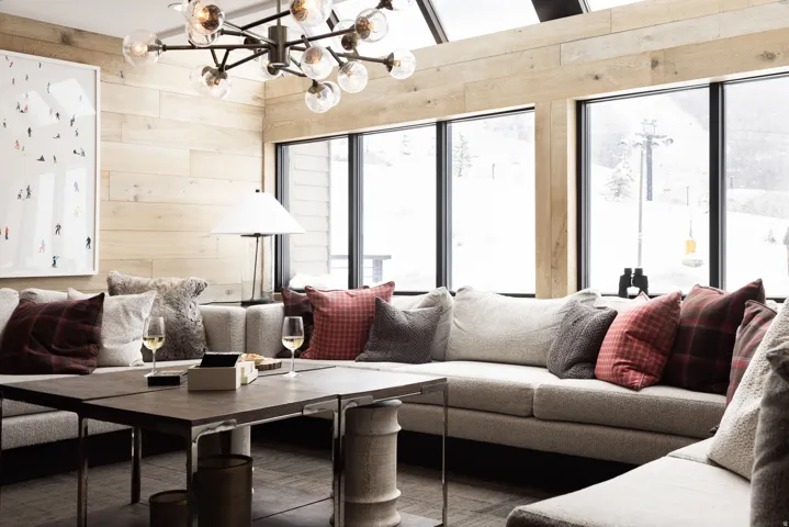 Open-concept living area featuring a vaulted ceiling with skylights, extensive wood-finish wall paneling, and large picture windows showcasing a snowy mountain landscape