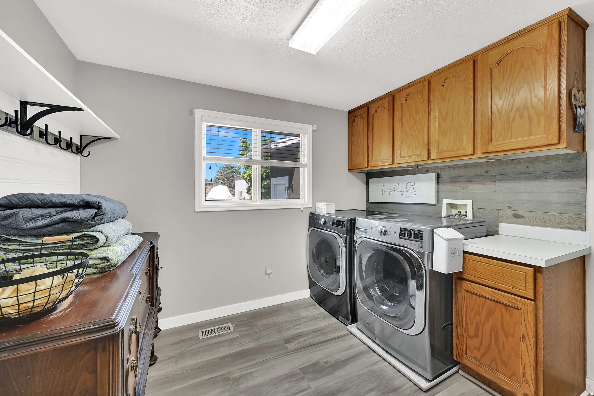 Dedicated laundry area featuring wood-finish flooring, a window providing natural light, upper and lower wood cabinetry, and a white countertop