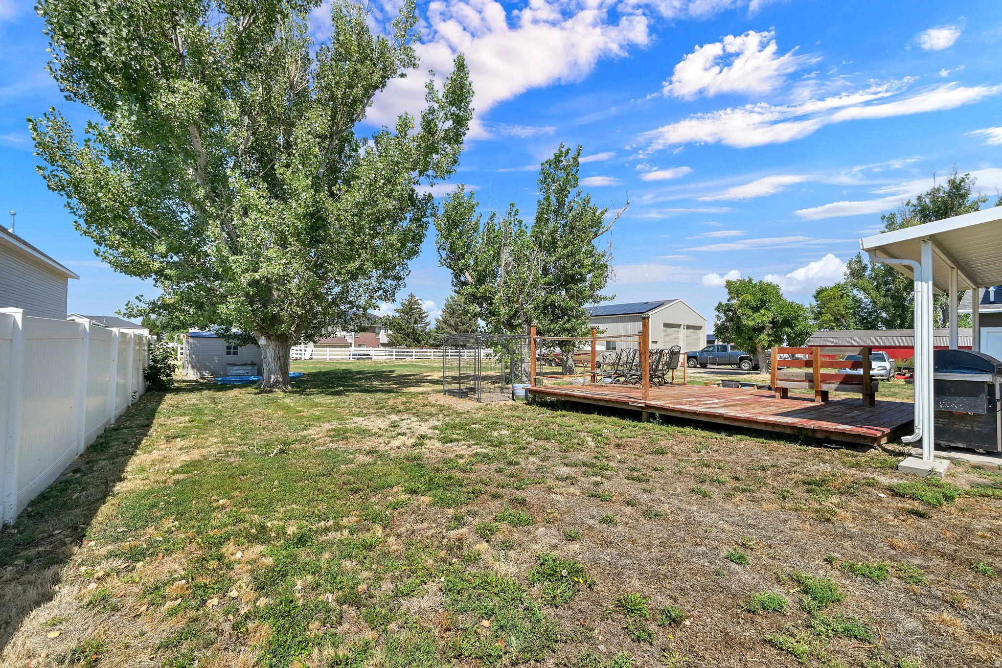 Expansive backyard featuring a wood deck with railing, a mature tree, and a white vinyl privacy fence