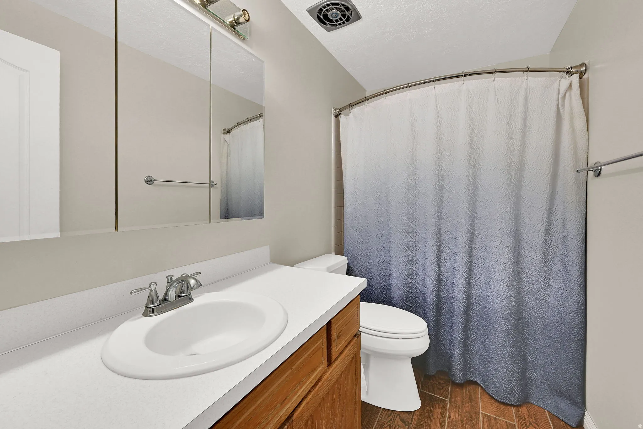 Bathroom featuring a wood-finish vanity with an integrated sink, a large mirror, and a shower with a curved rod