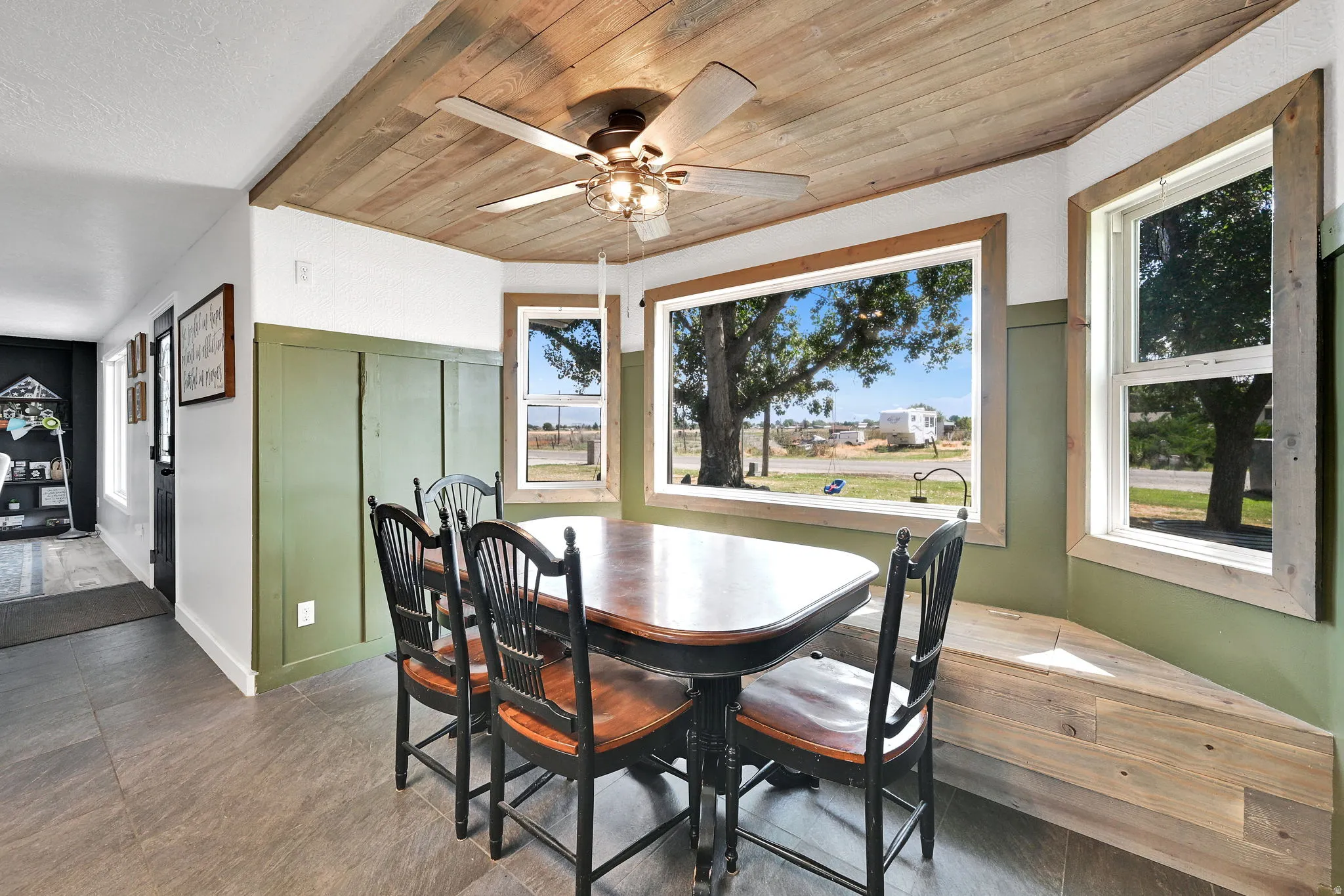 Breakfast nook featuring a wood-panel ceiling, ceiling fan with integrated lighting, wood-finish flooring, and green board and batten wainscoting