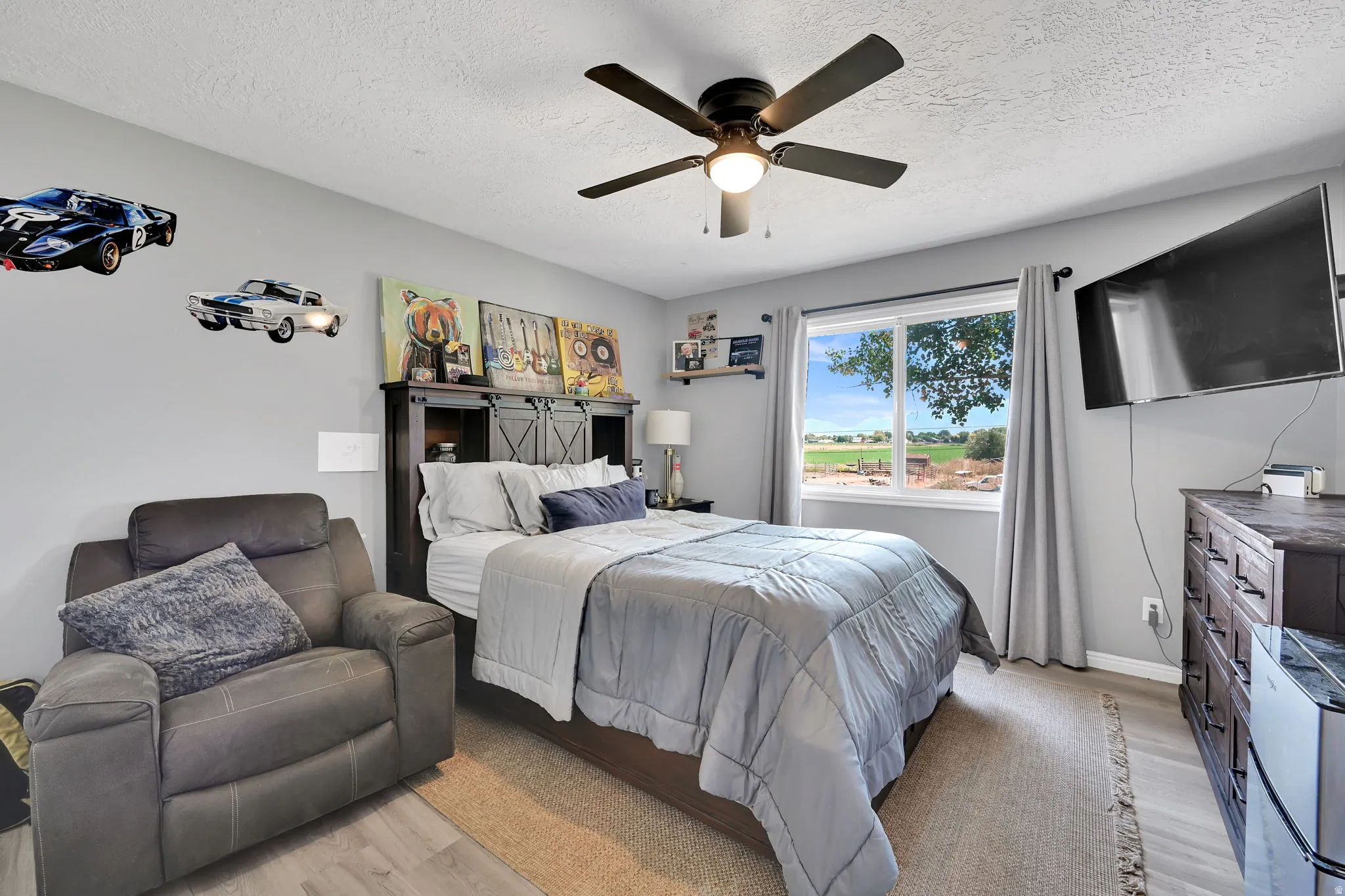 Bedroom featuring a ceiling fan with integrated lighting, a window with a rural outlook, and light gray wall paint