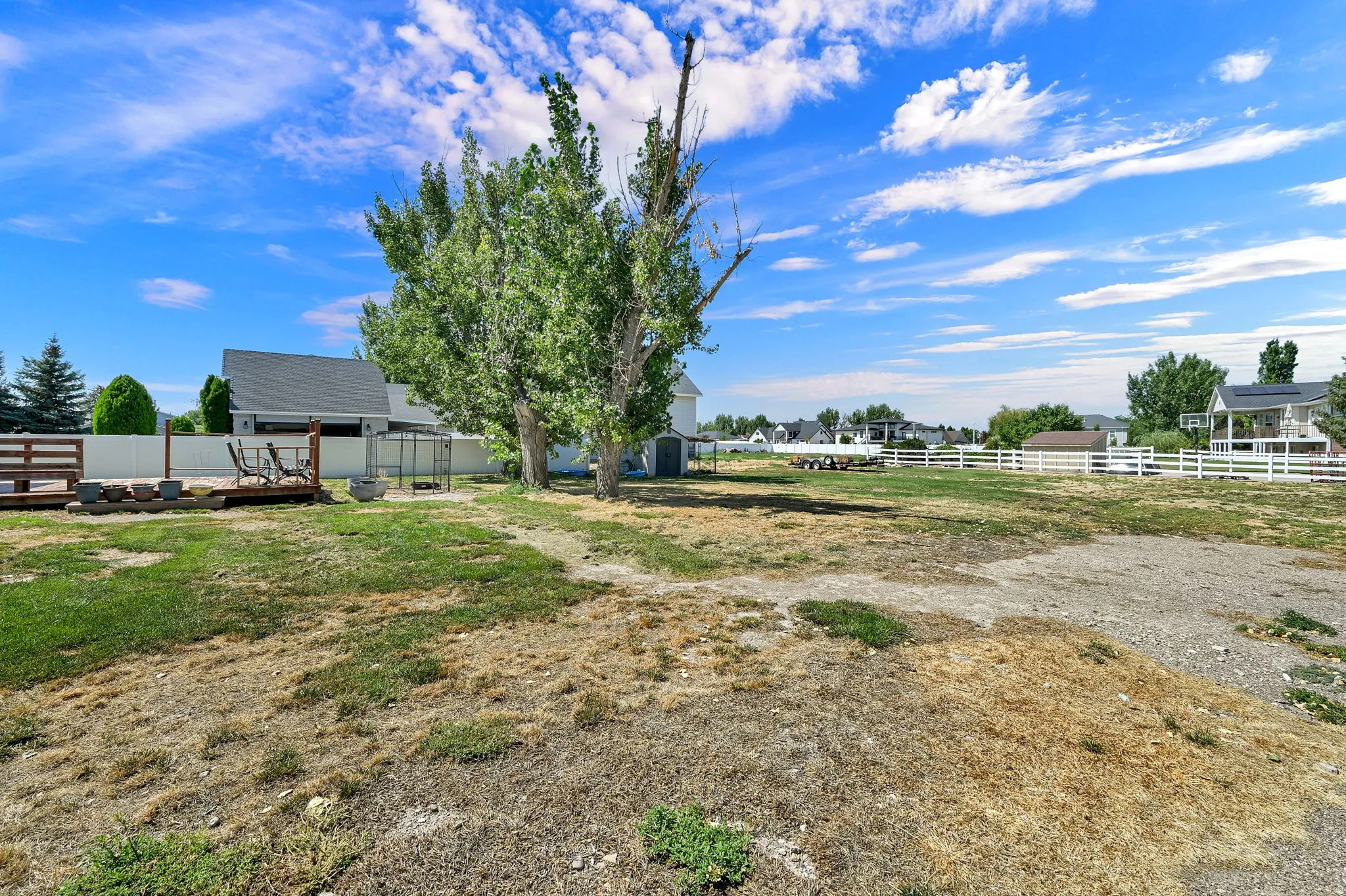 Expansive backyard featuring a white privacy fence, wood deck, and mature trees