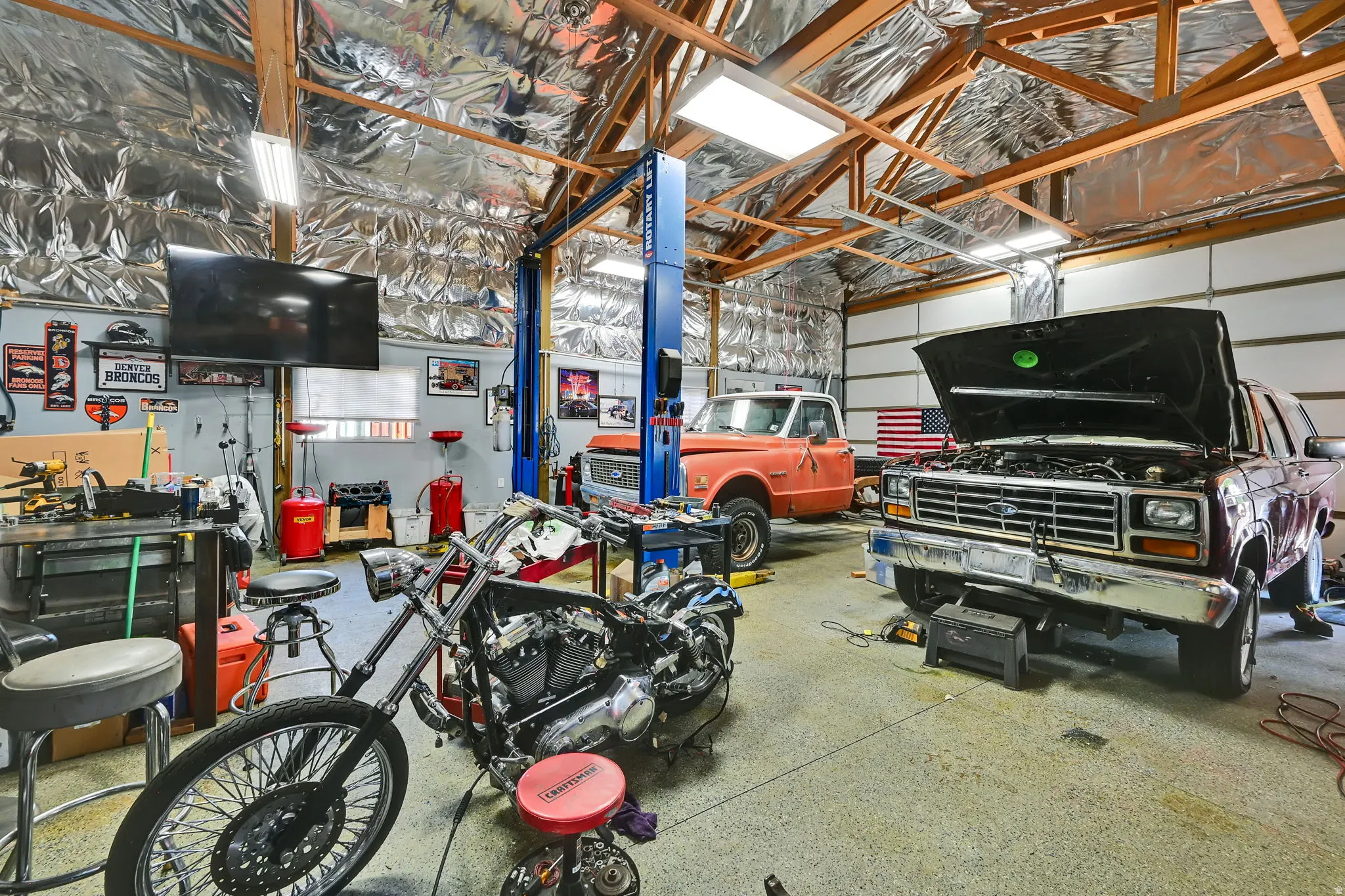 Spacious workshop with a vehicle lift, multiple garage doors, exposed wood beam ceiling, and overhead fluorescent lighting
