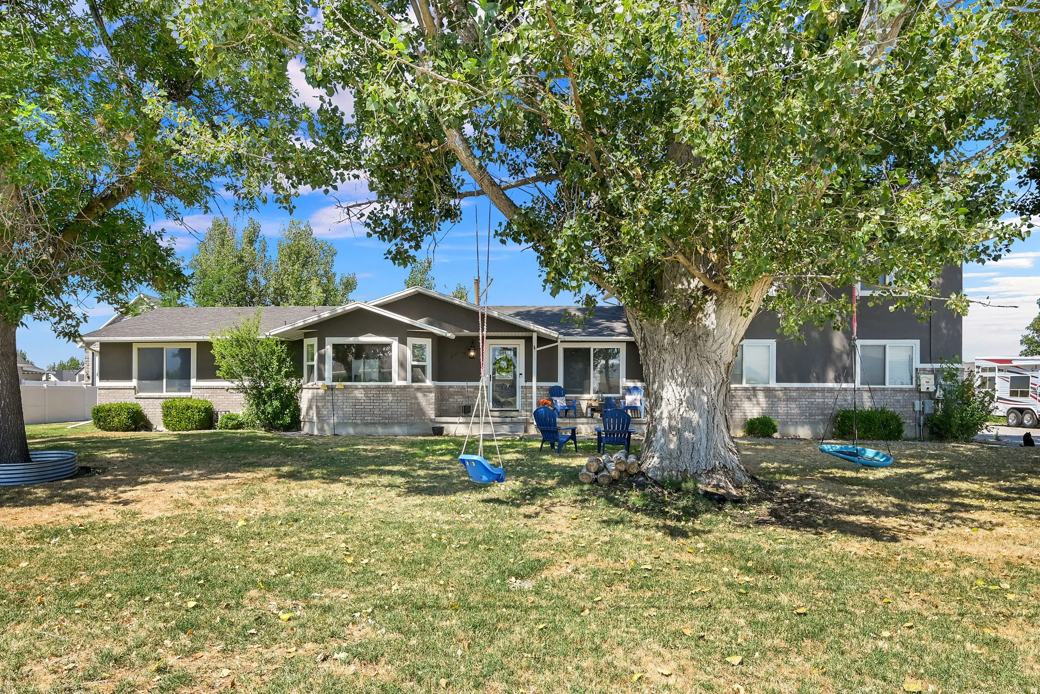Expansive front yard featuring mature shade trees, a well-maintained lawn, and a dark-toned exterior with light trim