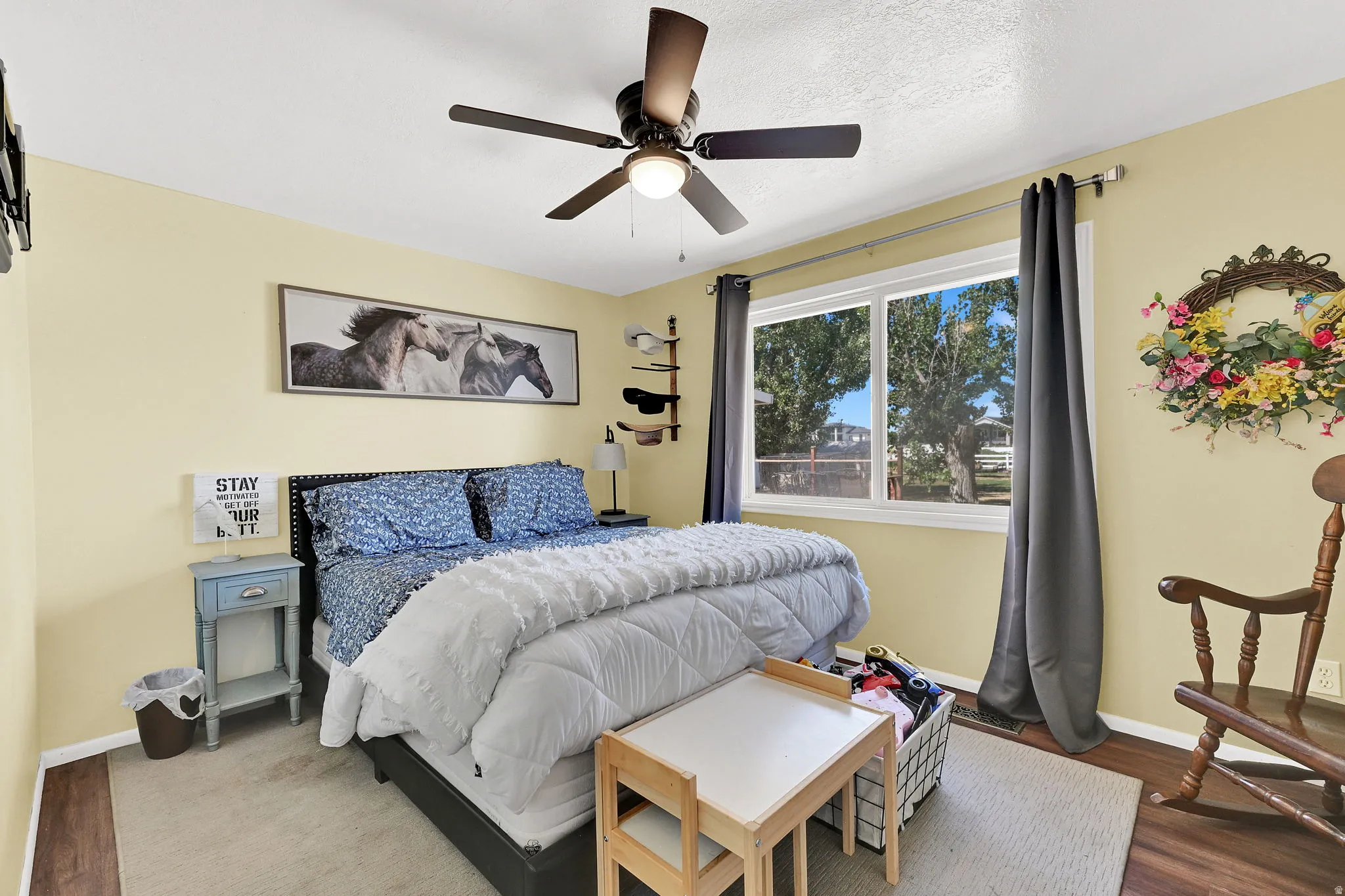 Spacious room featuring a ceiling fan with integrated lighting, a large window providing ample natural light, and dark wood-finish flooring complemented by an area rug