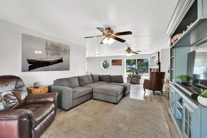 Open-concept living area featuring a large window, light-colored walls, wood-finish flooring, and multiple ceiling fans