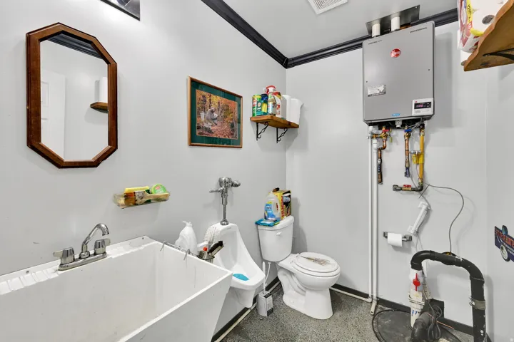 Utility space featuring a wall-mounted water heater, a porcelain toilet, and a wash basin with a chrome faucet