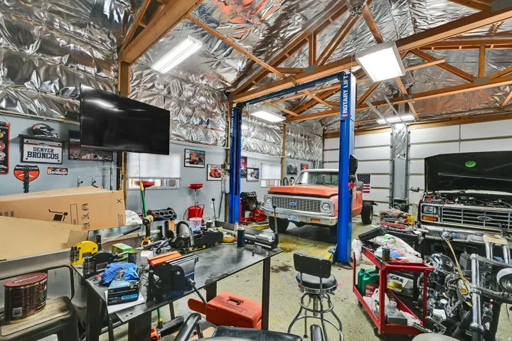 Spacious garage workshop featuring exposed wood beam ceilings, overhead fluorescent lighting, a built-in vehicle lift, and insulated walls