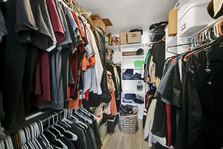 Walk-in closet featuring wood-finish flooring, built-in shelving, and multiple hanging rods for organization