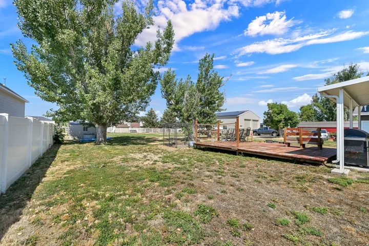 Expansive backyard featuring a wood deck with railing, a mature tree, and a white vinyl privacy fence