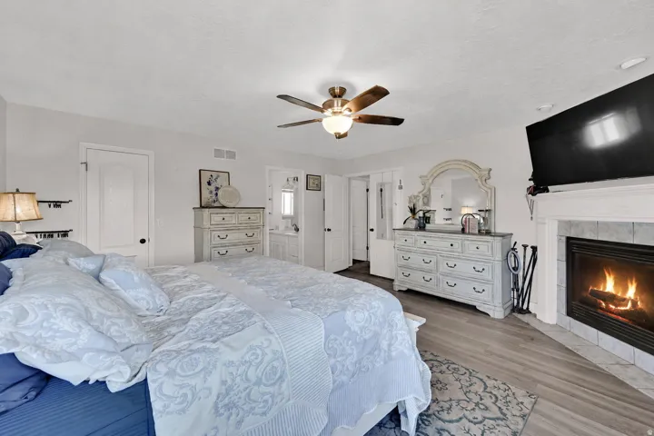 Spacious room featuring a fireplace with a stone surround, wood-finish flooring, a ceiling fan with integrated lighting, and multiple panel doors