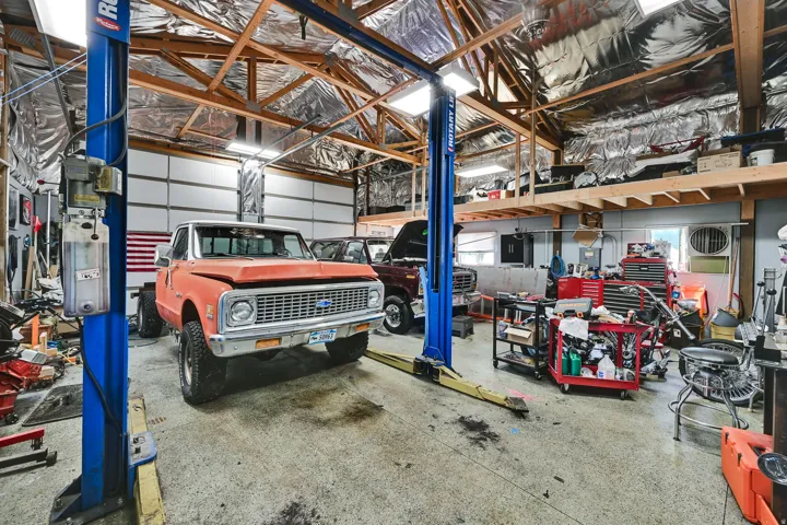 Spacious garage featuring a vehicle lift, exposed wooden truss ceiling, mezzanine storage, roll-up garage doors, and ample lighting