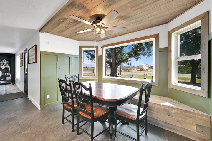 Breakfast nook featuring a wood-panel ceiling, ceiling fan with integrated lighting, wood-finish flooring, and green board and batten wainscoting