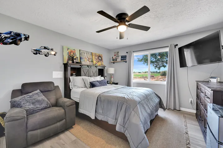 Bedroom featuring a ceiling fan with integrated lighting, a window with a rural outlook, and light gray wall paint