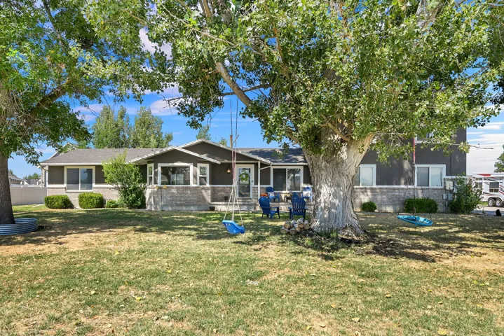 Expansive front yard featuring mature shade trees, a well-maintained lawn, and a dark-toned exterior with light trim