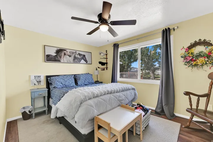 Spacious room featuring a ceiling fan with integrated lighting, a large window providing ample natural light, and dark wood-finish flooring complemented by an area rug