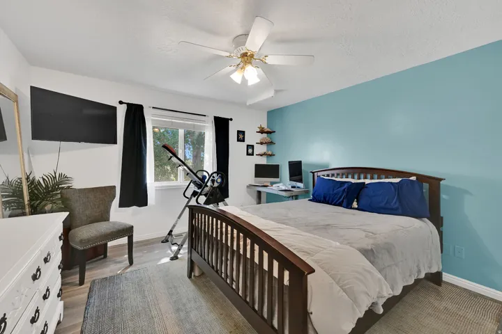Bedroom featuring an accent wall, wood-finish flooring, a ceiling fan with light fixture, and a window with black curtains