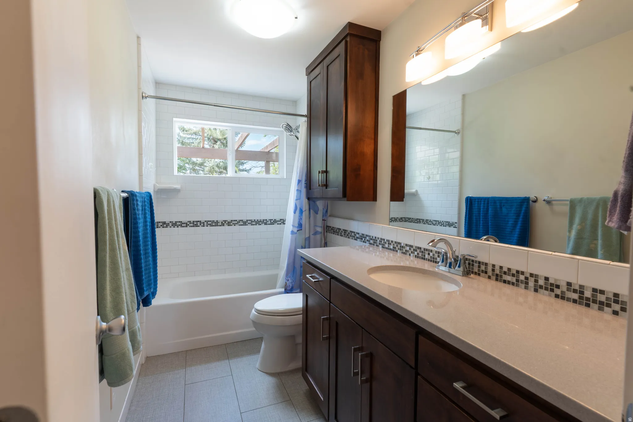 Bathroom featuring a modern vanity with light countertop, integrated sink, and dark wood-finish cabinetry. Love the window in the shower