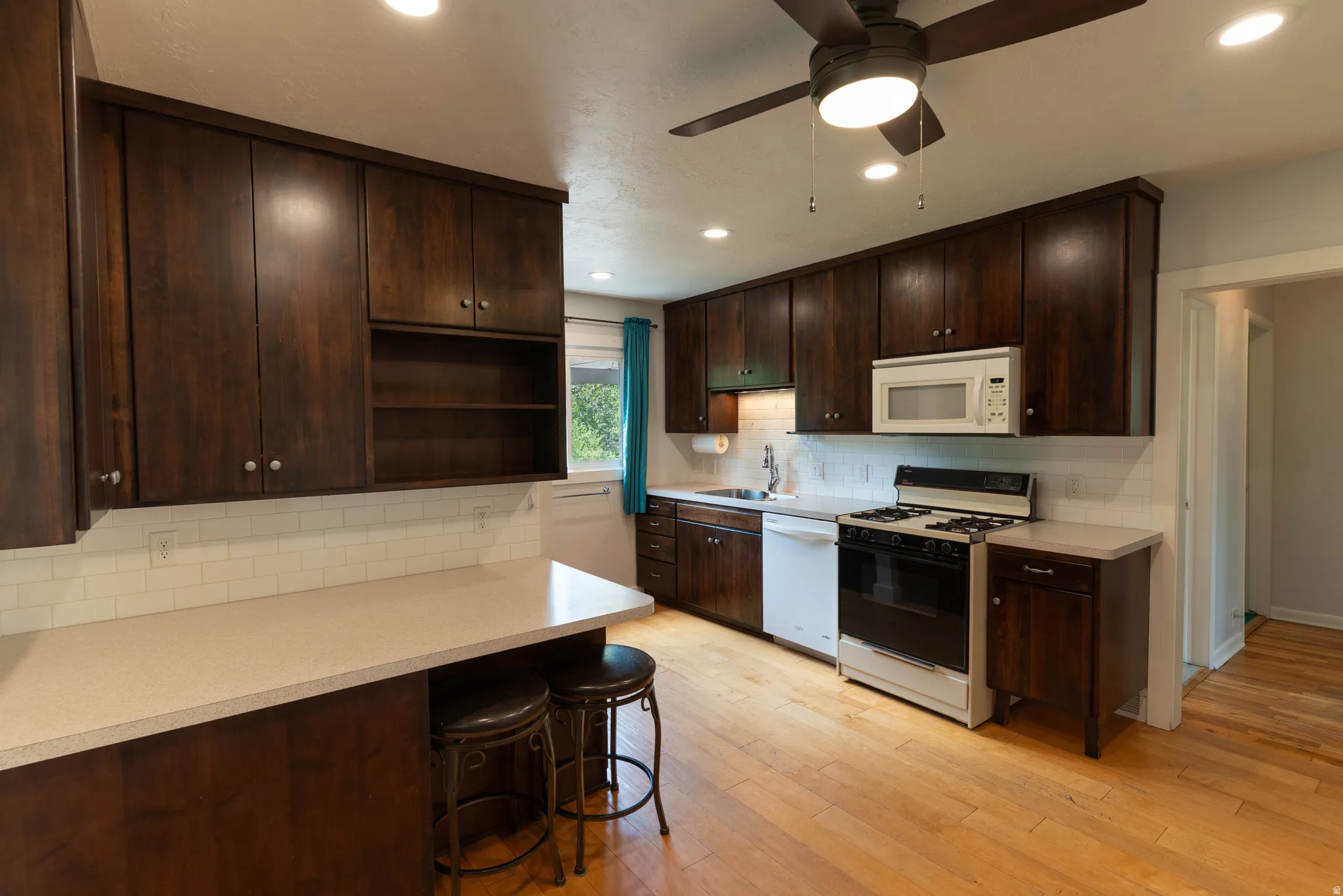 Kitchen featuring wood-finish flooring, dark wood cabinetry, and a white subway tile backsplash. Gas Range  Lots of storage