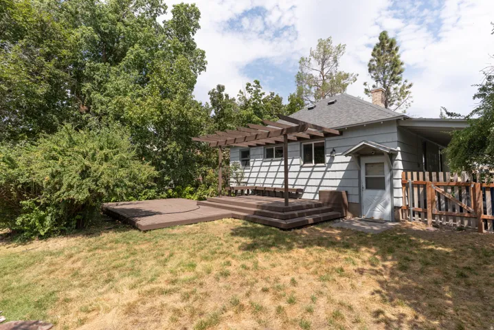 Rear exterior featuring wood siding, a multi-level deck with pergola, and mature trees