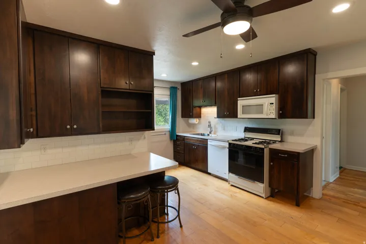 Kitchen featuring wood-finish flooring, dark wood cabinetry, and a white subway tile backsplash. Gas Range  Lots of storage